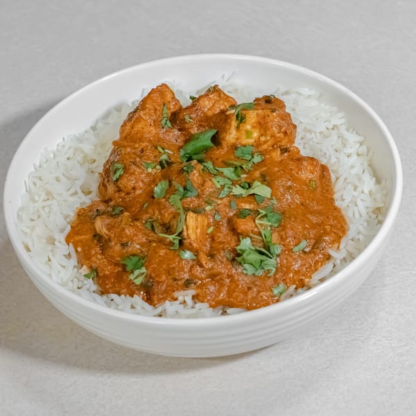 Bowl of white rice topped with creamy orange curry, chunky pieces, and fresh cilantro garnish.