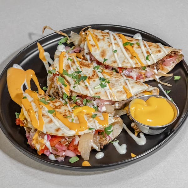 Grilled quesadilla wedges filled with meat and vegetables, drizzled with orange and white sauces, garnished with cilantro, and served with cheese sauce.