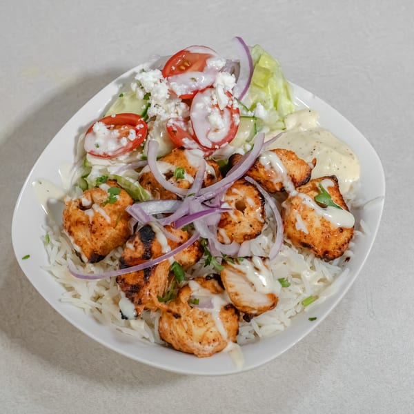 Grilled chicken pieces over white rice with lettuce, tomatoes, cucumbers, red onion, feta, and creamy dressing.