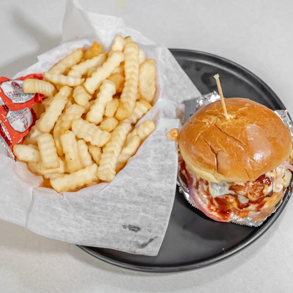 Cheeseburger with a glossy bun and crinkle-cut fries served on a black plate with ketchup packets.