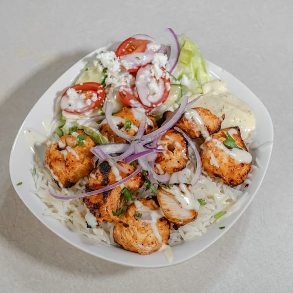 Grilled chicken pieces over white rice with lettuce, tomatoes, cucumbers, red onion, feta, and creamy sauce.