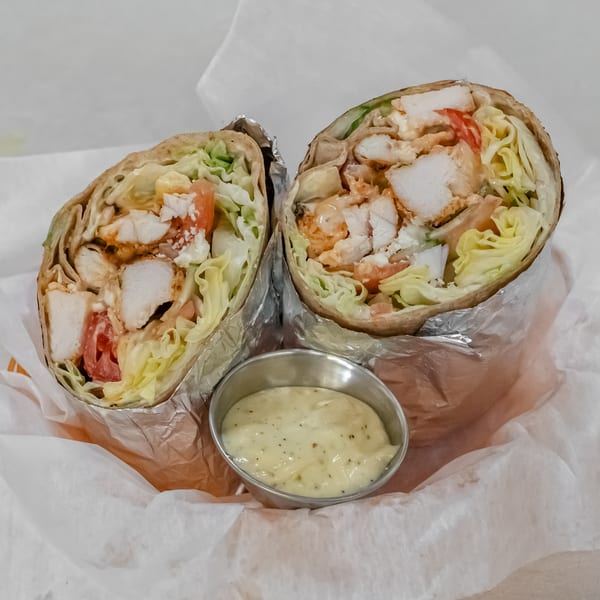 Two chicken wraps cut open to show lettuce, tomato, and creamy sauce, served with a side of dipping sauce.