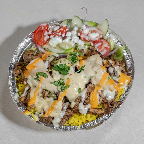 Mediterranean rice bowl topped with seasoned meat, lettuce, tomatoes, cucumbers, feta, herbs, and creamy sauces.