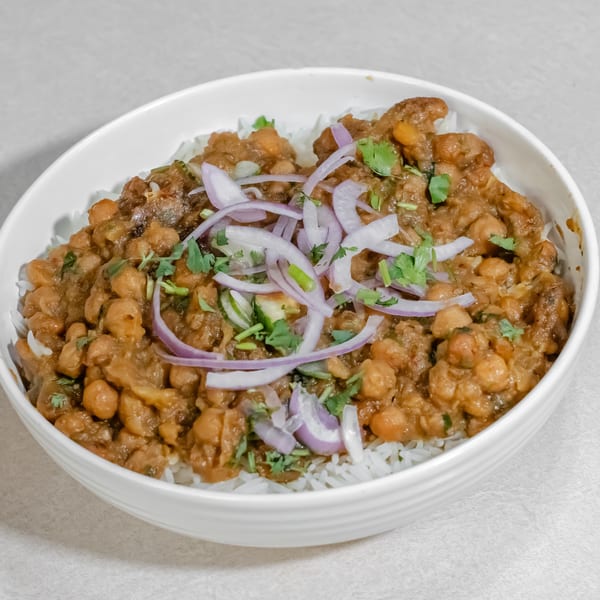 Bowl of spiced chickpea curry over white rice, topped with sliced red onions and fresh cilantro.